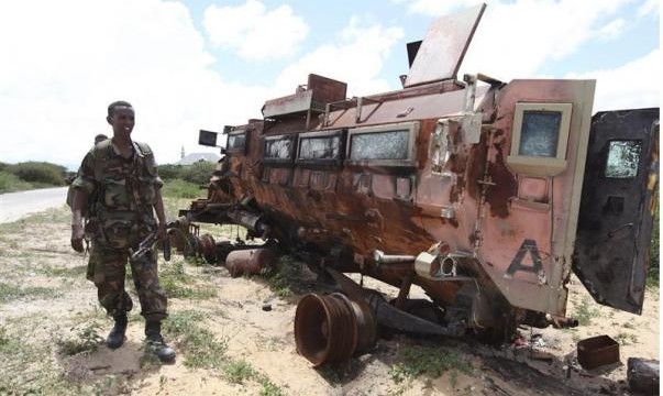 A Somali soldier looks at a burnt vehicle belonging to the AMISOM, as he patrols Dayniile district