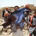 A man displays the bloodied shirt of a victim at the rubble of houses destroyed by an air strike in the Okash village near Sanaa