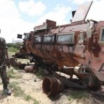 A Somali soldier looks at a burnt vehicle belonging to the AMISOM, as he patrols Dayniile district