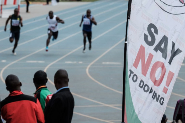 Athletes run as an anti doping banner is seen during the heat of the men's 100m at the Kenya National Trials at Kasarani Stadium in Nairobi on June 21, 2018, ahead of the 21st African Senior Championships in Nigeria to be held on August 1-5, 2018. / AFP PHOTO / Yasuyoshi CHIBA