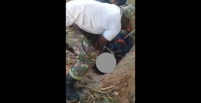 Uomo con uniforme militare sta decapitando un cadavere in una fossa comune a Cabo Delgado